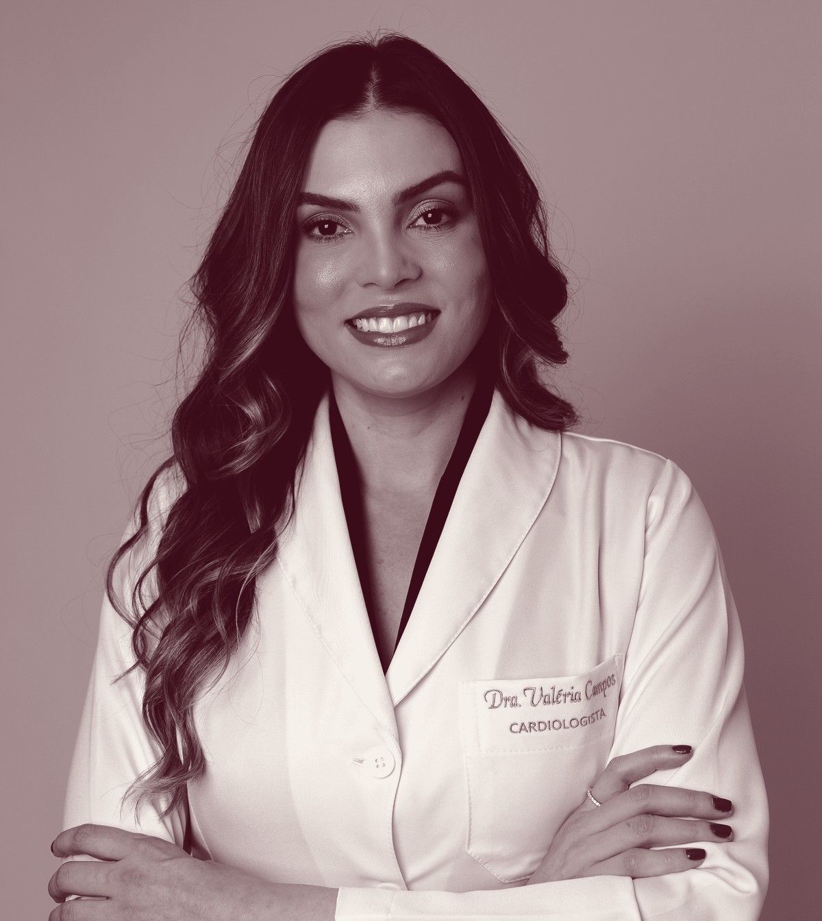 Dra. Valéria Campos de jaleco e braços cruzados, foto em tons de marsala